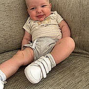 Theo is registered to the contest to win money with this photo: baby, smile, tongue_out, couch, comfortable, cute_clothing, white_shoes, happy, infant, person, indoor, texture, plush, seated, playful, young_child, casual, light, expression, home