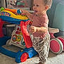 barefoot, carpet, child, colorful, curly_hair, furniture, happy, indoor, pants, person, pink_shirt, plastic, play, smiling, storage, toddler, toy, walker, wheel, zebra_print