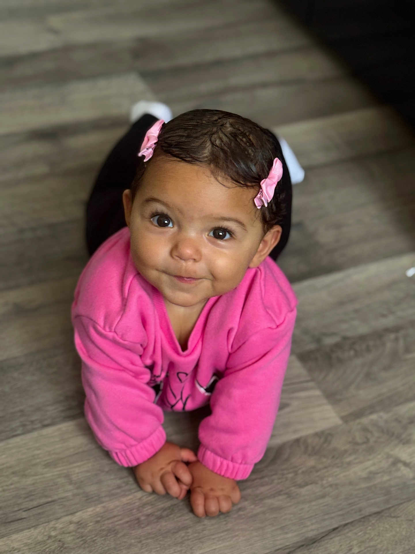 Juna a rejoint le concours — aidez-le/la à gagner de superbes lots ! baby, child, crawling, floor, wooden_floor, pink_sweater, pink_bows, hair, face, eyes, hands, indoor, person, infant, cute, smile, portrait, clothing, young_child, expression