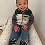 Gianni a rejoint le concours — aidez-le/la à gagner de superbes lots ! casual_clothing, child, cozy, cushion, face, fleece_jacket, hands, happy, indoor, jeans, nike, pattern, portrait, shoes, sitting, smiling, sneakers, toddler, wooden_frame, young_child