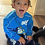 blue_sweatshirt, cartoon_character, casual, child, clothing, cute, expression, floor, hair, happy, indoor, person, playful, portrait, sitting, smiling, sneakers, toddler, tongue_out, young