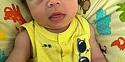 Yésiah is registered to the contest to win money with this photo: baby, infant, child, yellow_clothing, sunglasses_print, curly_hair, blue_eyes, cushion, animal_print, colorful, indoors, portrait, cute, resting, closeup, soft_lighting, expression, skin, young, person