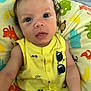 baby, infant, child, yellow_clothing, sunglasses_print, curly_hair, blue_eyes, cushion, animal_print, colorful, indoors, portrait, cute, resting, closeup, soft_lighting, expression, skin, young, person