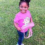 Arianna is registered to the contest to win money with this photo: child, girl, smiling, outdoor, grass, greenery, pink_shirt, jeans, sneakers, purse, hair_buns, happy, cute, person, standing, nature, daylight, casual_clothing, young_child, playful