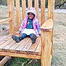 Arianna joined the competition — help win amazing prizes! child, toddler, smiling, jacket, boots, wooden_chair, outdoor, grass, farm, oversized_object, happy, person, nature, playful, winter_clothing, seat, wood, big_chair, cute, portrait
