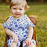 toddler, child, baby, blue_bow, floral_outfit, barefoot, wooden_chair, smiling, outdoor, grass, portrait, cute, young_child, blue_eyes, short_hair, sitting, sunlight, nature, happy, summer