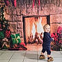 child, toddler, baby, fireplace, presents, gifts, christmas_tree, stockings, decorations, stone_wall, tiles, floor, backdrop, holiday, festive, indoor, cozy, shoes, blue_outfit, portrait