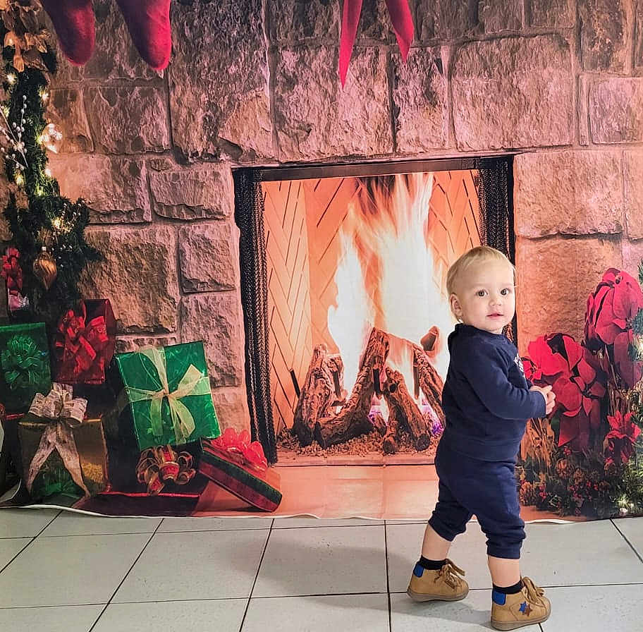 Alessandro participe au concours pour gagner de l'argent avec cette photo : child, toddler, baby, fireplace, presents, gifts, christmas_tree, stockings, decorations, stone_wall, tiles, floor, backdrop, holiday, festive, indoor, cozy, shoes, blue_outfit, portrait