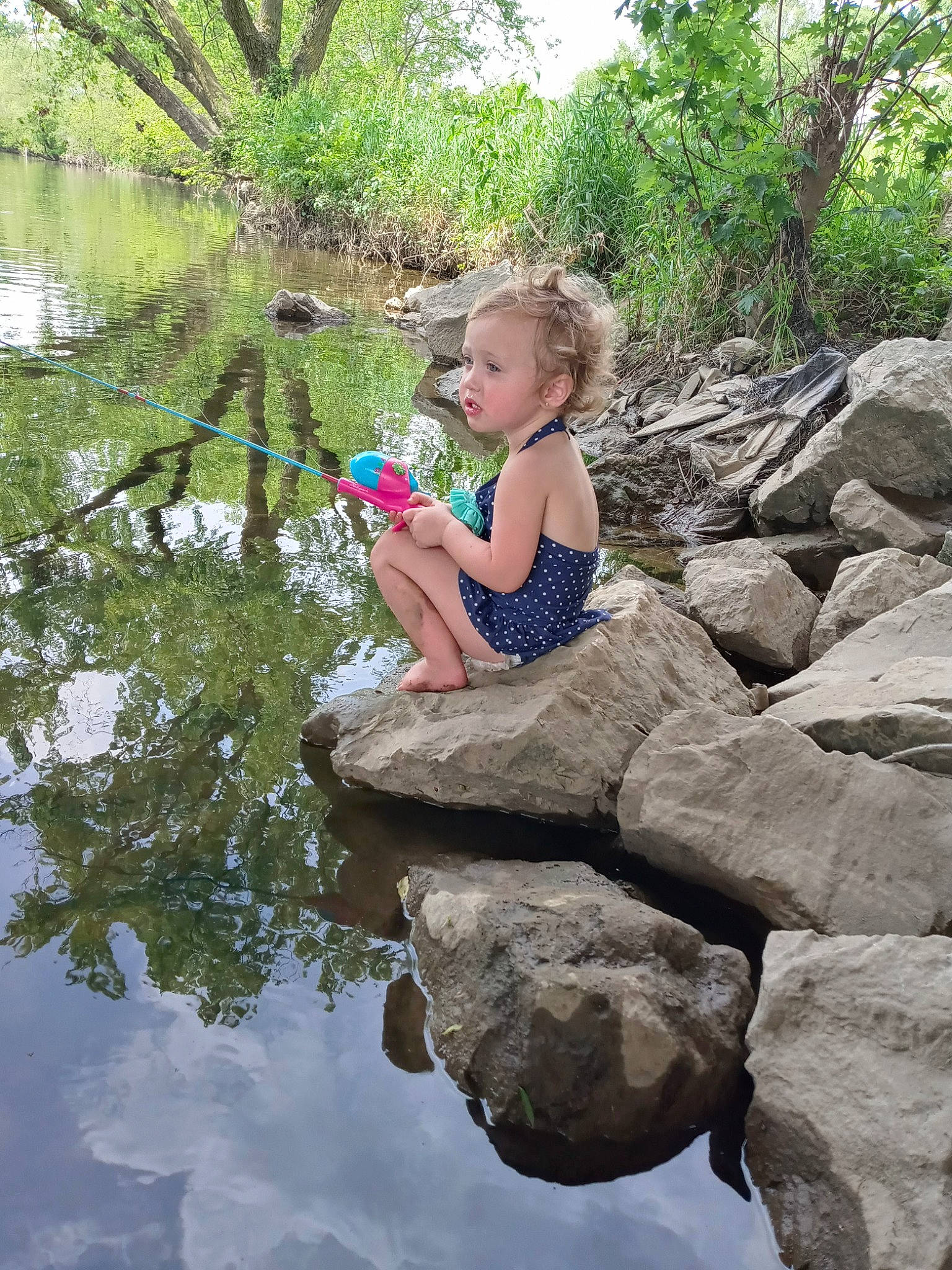 Emmariah is registered to the contest to win money with this photo: bank, bedrock, creek, forest, fun, grass, hand, lake, landscape, leisure, mammal, people_in_nature, person, plant, recreation, stream, toddler, tree, water, water_resources