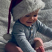 Lenny participe au concours pour gagner de l'argent avec cette photo : baby, child, santa_hat, smiling, cute, indoor, plush, holiday, festive, portrait, happy, infant, cozy, blanket, foot, hand, clothing, cute_expression, sitting, soft_lighting