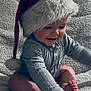 baby, child, santa_hat, smiling, cute, indoor, plush, holiday, festive, portrait, happy, infant, cozy, blanket, foot, hand, clothing, cute_expression, sitting, soft_lighting