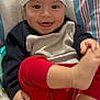 baby, smiling, hat, red_pants, barefoot, blanket, striped_blanket, infant, cute, playful, child, person, happy, young_child, indoors, cozy, clothing, face, foot, sitting
