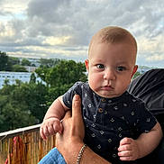 Kenan a rejoint le concours — aidez-le/la à gagner de superbes lots ! baby, child, person, face, hand, clothing, bracelet, blue_jeans, outdoor, balcony, sky, clouds, trees, nature, portrait, expression, anchor_pattern, holding, adult_hand, casual