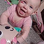 Bella is registered to the contest to win money with this photo: baby, smiling, blue_eyes, pink_clothing, toy, carpet, indoor, child, happy, playful, face, person, infant, cute, cheek_mark, baby_gear, floor, colorful, closeup, young_child