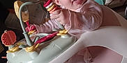 Bella joined the competition — help win amazing prizes! baby, child, infant, pink_clothing, toy, activity_seat, smiling, happy, indoor, carpet, face, hand, play, seat, furniture, person, cute, young_child, expression, colorful