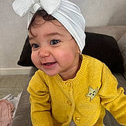 Loëlya a rejoint le concours — aidez-le/la à gagner de superbes lots ! baby, bow, child, clothing, couch, cushion, cute, eyes, face, headwrap, indoor, playful, portrait, sitting, smiling, sweater, teeth, toddler, white_bow, yellow_sweater