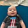baby, clothing, couch, cushion, face, flag, furniture, happy, head, homedecor, newborn, pants, person, photography, portrait, quilt, shirt, sitting, smile, t_shirt