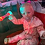 toddler, child, pacifier, pajamas, pink_bow, toy_wand, glowing_toy, red_chair, indoor, people, adult, seated, blurred_background, face, footwear, cute_socks, light_effect, person, young_child, playing