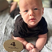 Ryker is registered to the contest to win money with this photo: baby, infant, child, black_clothing, face, hands, blanket, wooden_sign, milestone, lying_down, portrait, indoors, soft_light, closeup, cute, expression, skin, head, young, person
