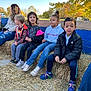 children, kids, hay_bales, fall, autumn, outdoor, trees, jackets, sneakers, grass, blue_sky, bench, playful, friends, casual, smiling, nature, daylight, leaves, group