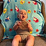 armchair, baby, bare_feet, blanket, chair, child, colorful, fish_pattern, furniture, gray_outfit, home, indoors, infant, looking_at_camera, milestone, open_mouth, portrait, sitting, smiling, wooden_sign