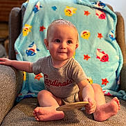 Grayson joined the competition — help win amazing prizes! armchair, baby, barefoot, blanket, cardinals_shirt, child, colorful, cozy, fish_pattern, furniture, happy, indoors, infant, living_room, portrait, seated, sitting, smiling, sports_shirt, wooden_object