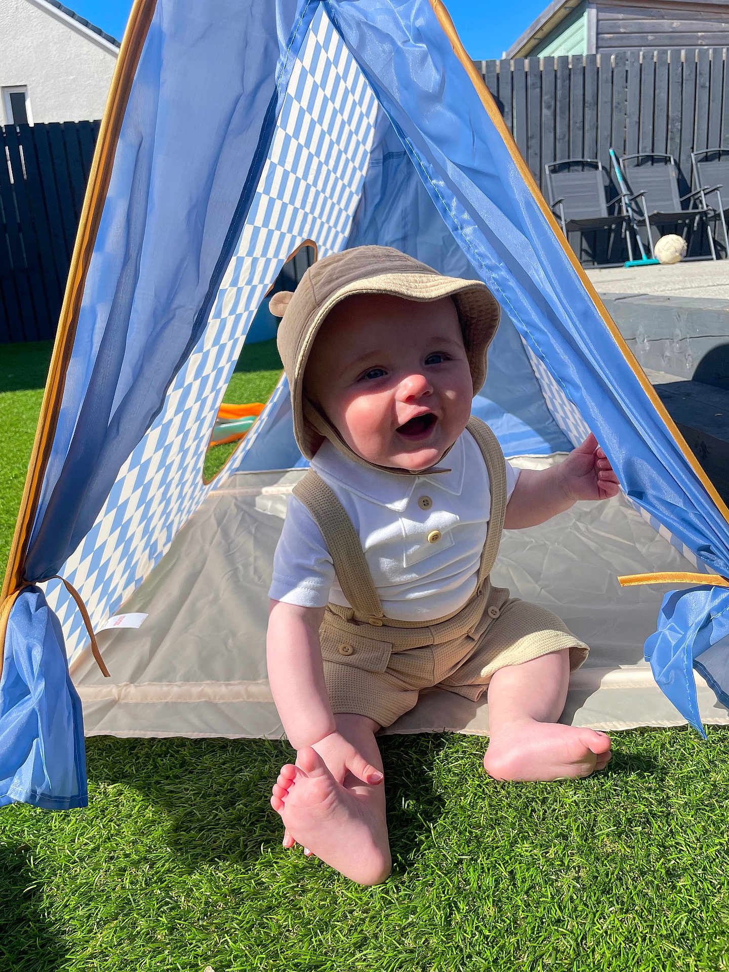 Ollie joined the competition — help win amazing prizes! baby, child, tent, hat, grass, outdoor, sunlight, smiling, sitting, clothing, beige, blue, white, checkered, foot, hand, playful, happy, person, summer