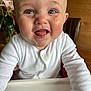baby, child, smiling, happy, face, white_clothing, highchair, tongue_out, indoor, wooden_furniture, flower_vase, closeup, cute, infant, skin, person, portrait, table, expressive, young