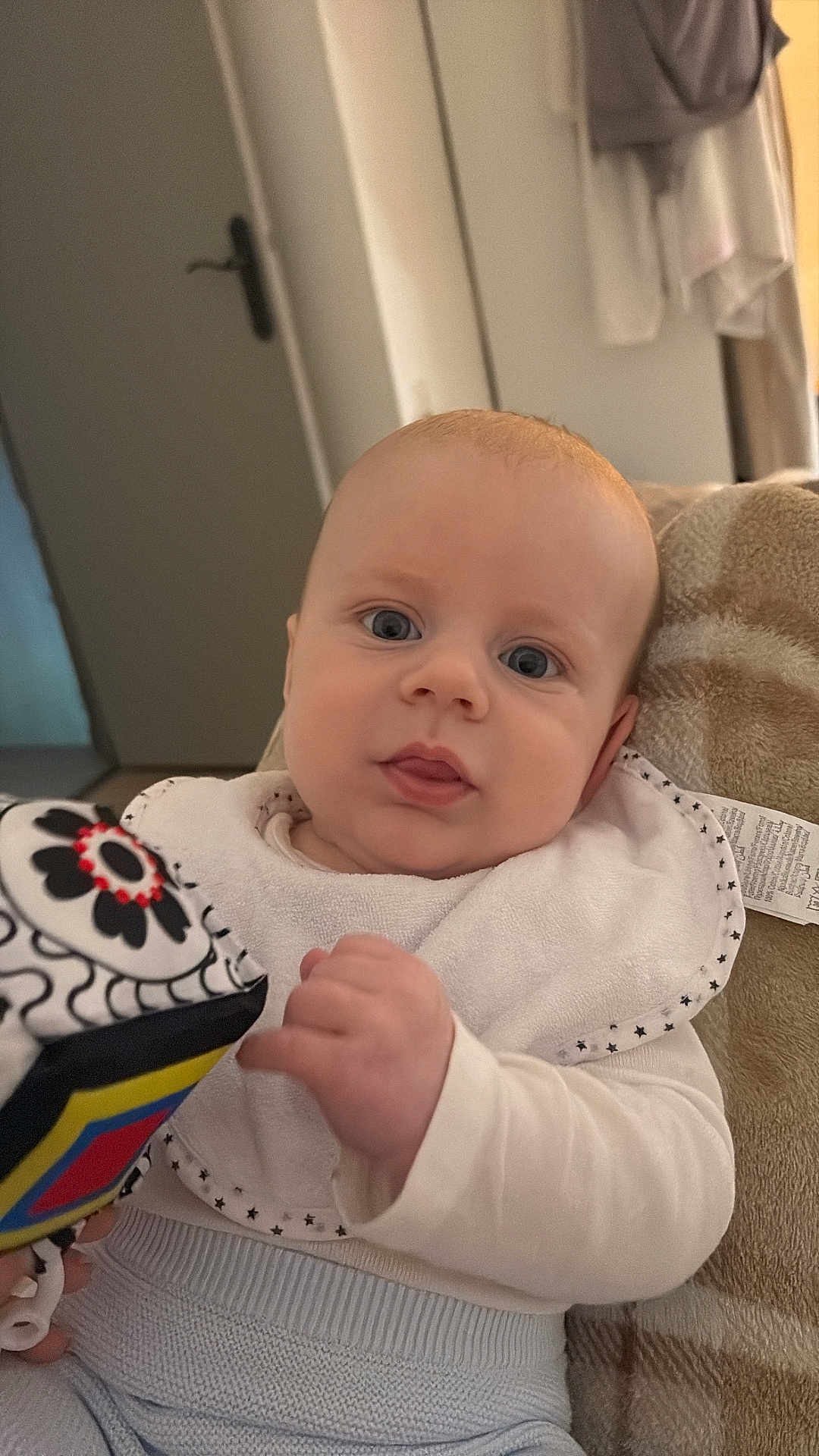 Liam a rejoint le concours — aidez-le/la à gagner de superbes lots ! baby, infant, toy, bib, white_clothing, blue_eyes, hand, face, indoor, blanket, soft_toy, curious, young_child, portrait, cozy, seated, home, closeup, cute, child