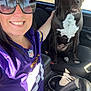 Cooper joined the competition — help win amazing prizes! woman, dog, car, sunglasses, purple_jersey, smiling, seat, steering_wheel, parking_lot, daylight, hand, pet, vehicle_interior, black_dog, white_markings, casual, portrait, friendship, happy, indoor