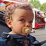 Maël a rejoint le concours — aidez-le/la à gagner de superbes lots ! toddler, child, pacifier, blue_eyes, curly_hair, stroller, straps, outdoor, carnival, background_blur, person, cute, face, clothing, daylight, portrait, baby, expression, seat, playful
