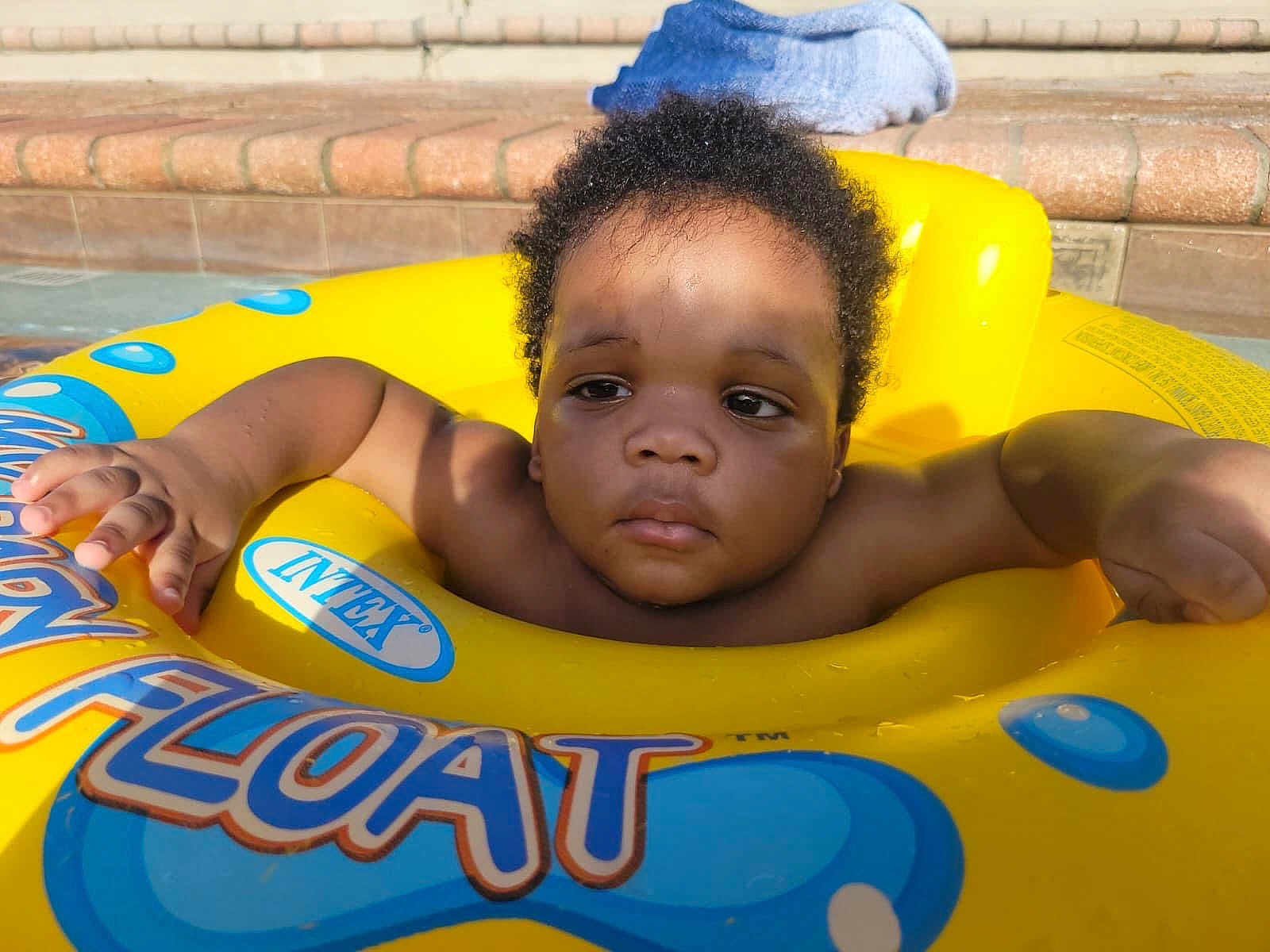 Jevaughn is registered to the contest to win money with this photo: baby, child, pool, float, yellow, water, toddler, swimming, outdoor, sunlight, shadow, towel, steps, skin, curly_hair, relaxation, summer, play, fun, infant