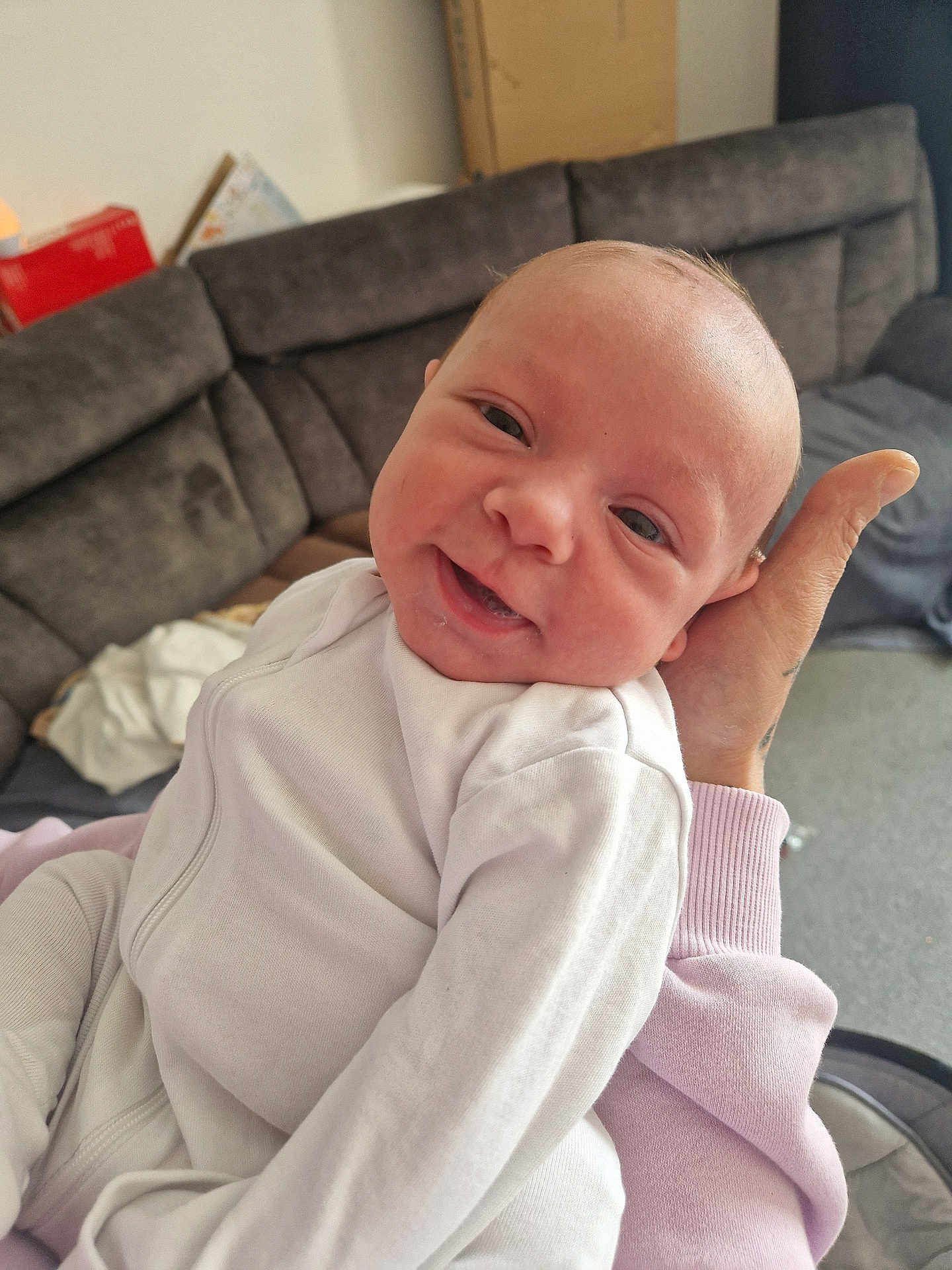 Beau is registered to the contest to win money with this photo: baby, infant, smile, white_clothing, hand, couch, living_room, person, face, indoor, soft_light, cozy, newborn, portrait, human, happy, sitting, casual, child, parent
