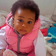 Aelya a rejoint le concours — aidez-le/la à gagner de superbes lots ! baby, infant, pink_vest, white_sleeves, curly_hair, sitting, blanket, soft_toys, indoor, cute, child, portrait, playful, closeup, floor, clothing, footwear, expression, home, young_child