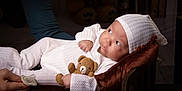 Abisai joined the competition — help win amazing prizes! baby, infant, teddy_bear, pacifier, white_clothing, hat, cushion, hand, indoor, portrait, cute, knitwear, sleepwear, child, soft_lighting, cozy, resting, looking_away, wooden_furniture, warm_colors