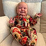 baby, child, smile, floral_clothing, onesie, chair, cozy, happy, infant, portrait, indoor, plush, relaxing, cute, person, sitting, comfortable, soft, face, fingers