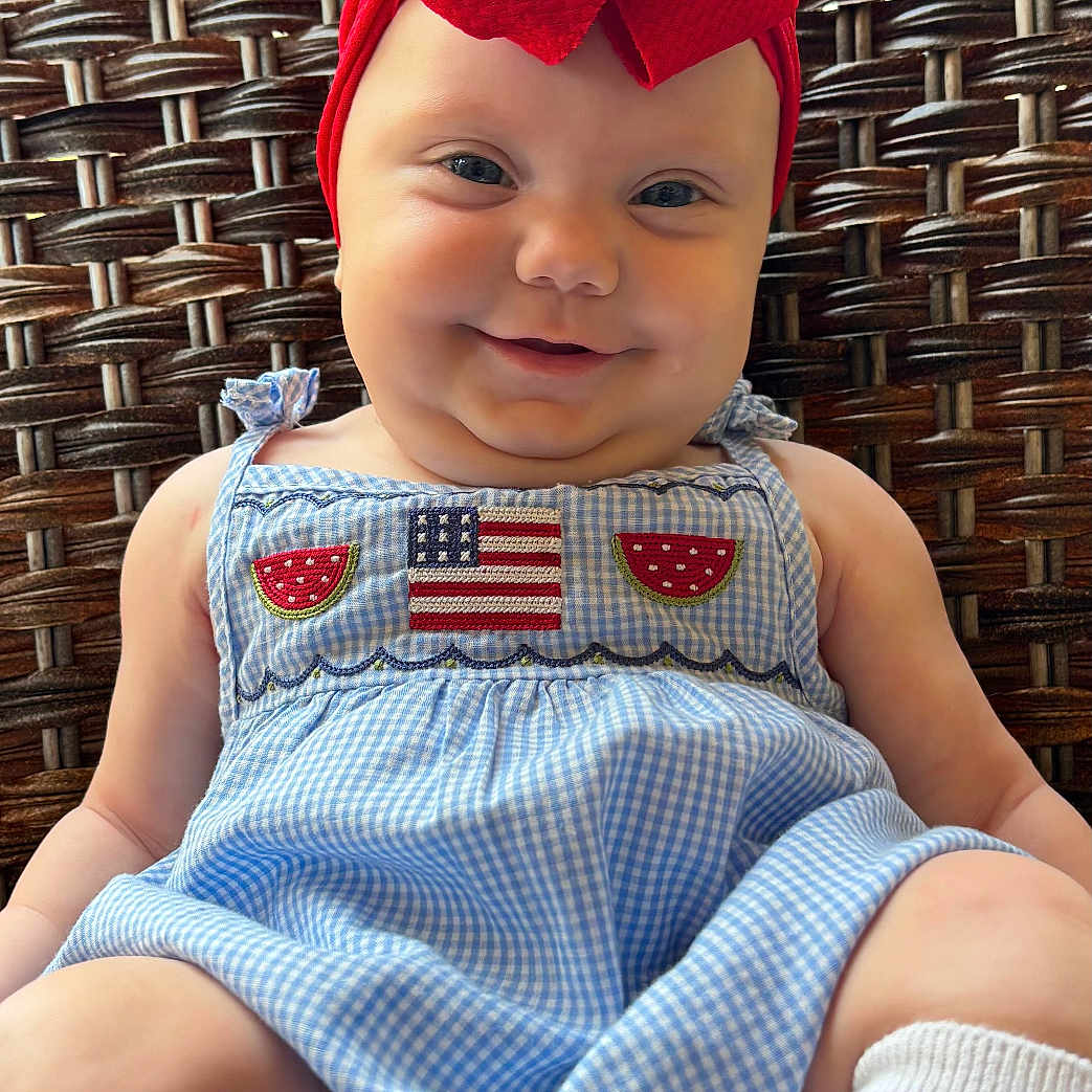 Loralie is registered to the contest to win money with this photo: baby, child, smiling, red_bow, headband, blue_dress, gingham, american_flag_patch, watermelon_patch, sitting, woven_chair, white_socks, cute, portrait, infant, happy, closeup, outdoor, fashion, adorable