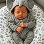 baby, sleeping, onesie, elephant_costume, hood, ears, trunk, cushion, floral_pattern, gray, soft_lighting, peaceful, infant, cute, cozy, hands, feet, portrait, indoors, comfortable