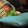 baby, green_shirt, blue_pillow, couch, infant, person, indoor, child, diaper, curious, soft_lighting, tattoo, seated_adult, black_hair, skin, furniture, relaxed, home, casual, comfort