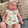 Faith joined the competition — help win amazing prizes! baby, infant, child, romper, headband, bow, floral_pattern, pillow, couch, fabric, skin, cute, tongue_out, sitting, indoors, soft_lighting, portrait, happy, plush, comfort