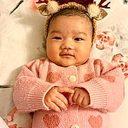 Saachi is registered to the contest to win money with this photo: baby, infant, child, pink_sweater, heart_pattern, reindeer_headband, red_bow, hands, face, smile, lying_down, blanket, floral_pattern, cute, adorable, indoors, portrait, young_child, cozy, warm_clothing