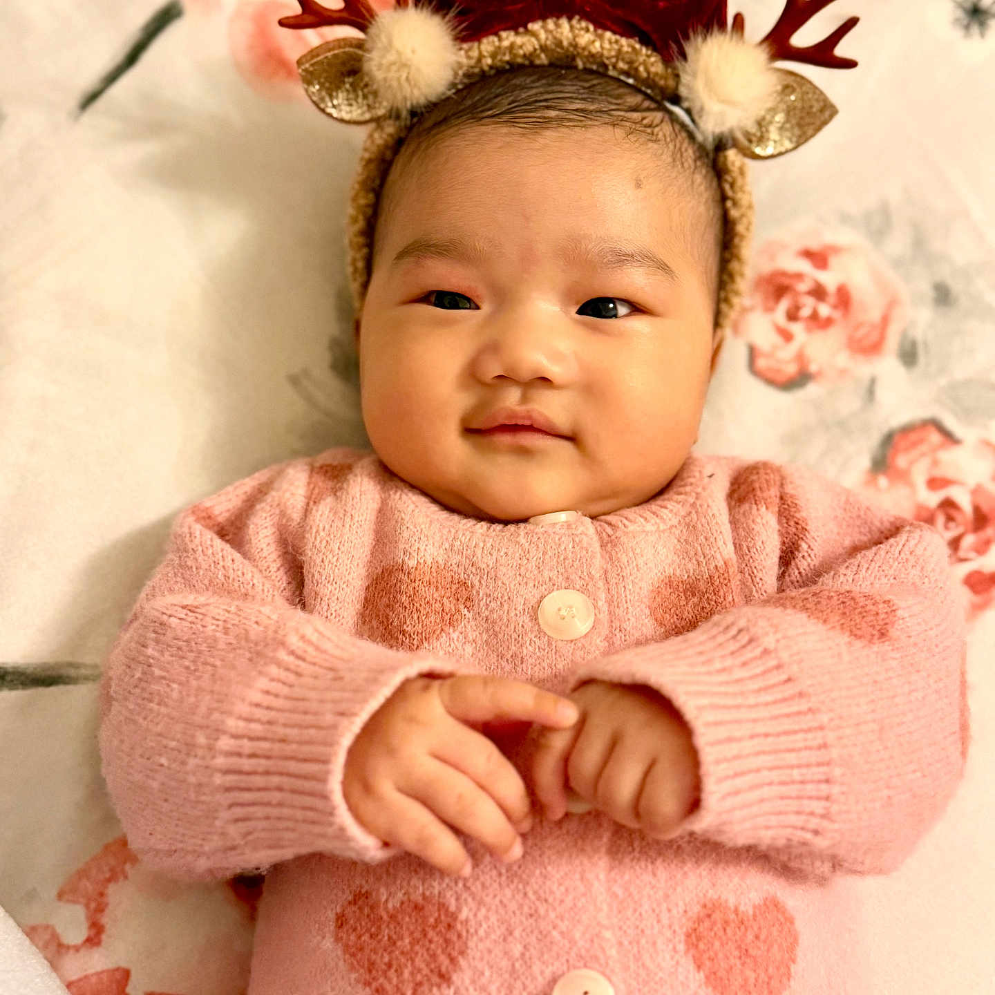 Saachi is registered to the contest to win money with this photo: adorable, baby, blanket, child, cozy, cute, face, floral_pattern, hands, heart_pattern, indoors, infant, lying_down, pink_sweater, portrait, red_bow, reindeer_headband, smile, warm_clothing, young_child