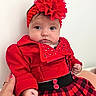baby, child, red_clothing, headband, flower, face, hand, plaid_skirt, jacket, cute, portrait, indoor, infant, person, fashion, accessory, pink_nail_polish, holding, soft_light, closeup