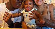 Amoni is registered to the contest to win money with this photo: affection, baby, casual_clothing, curly_hair, family, father, happy, holding, indoor, joy, menu, mother, napkin, people, portrait, restaurant, smile, table, tattoo, wooden_table