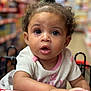 Zanova joined the competition — help win amazing prizes! baby, child, shopping_cart, grocery_store, curly_hair, wide_eyes, pink_clothing, hand, aisle, blurred_background, face, portrait, infant, expression, cute, indoor, person, focus, curiosity, cart_handle