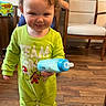 toddler, child, baby_bottle, green_pajamas, smile, indoor, wooden_floor, chair, person, face, curly_hair, room, furniture, lunchbox, toy, happy, clothing, standing, cute, playful