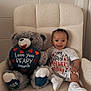 baby, teddy_bear, chair, plush, smiling, white_clothing, sneakers, celebration, heart, cute, indoor, child, happy, gift, love, cozy, portrait, infant, sitting, cute_outfit