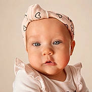 Ariella is registered to the contest to win money with this photo: baby, child, face, headband, pink, heart_pattern, blue_eyes, close_up, portrait, cute, infant, soft_lighting, neutral_background, ruffled_clothing, skin, person, young_child, expression, apparel, headwear