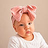baby, infant, child, headband, pink_bow, white_shirt, portrait, closeup, cute, chubby_cheeks, soft_lighting, neutral_background, innocent, gaze, face, person, young_child, studio_photo, adorable, expression