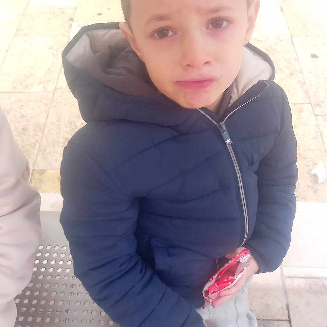 Yassine participe au concours pour gagner de l'argent avec cette photo : bench, boy, casual_clothing, child, daylight, expression, hood, jacket, outdoor, pavement, person, pout, red_socks, sad, shoes, snack, sweatpants, urban, waiting, wrapper